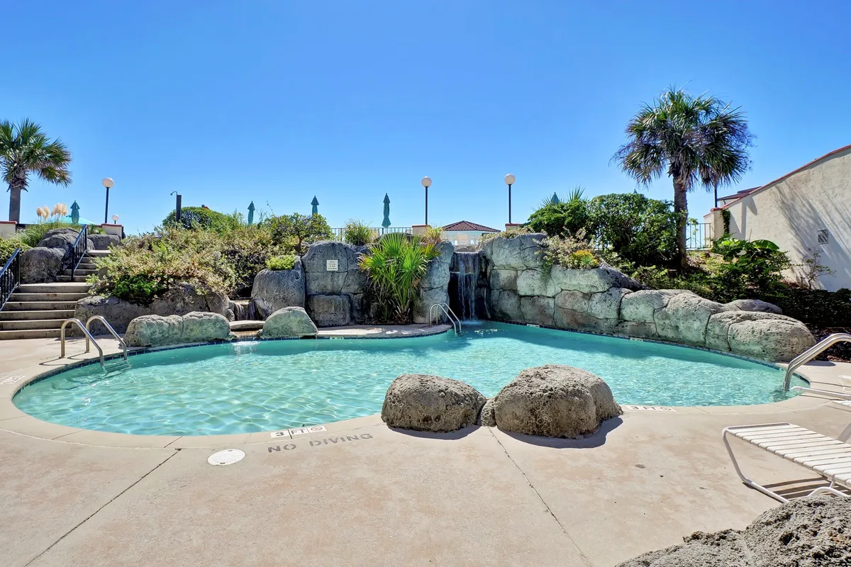 This image depicts a vibrant resort swimming pool surrounded by rock formations, lush greenery, and poolside lounge chairs. Guests are shown swimming, sunbathing, or relaxing in a tranquil and refreshing atmosphere that captures the heart of the resort's recreational amenities.