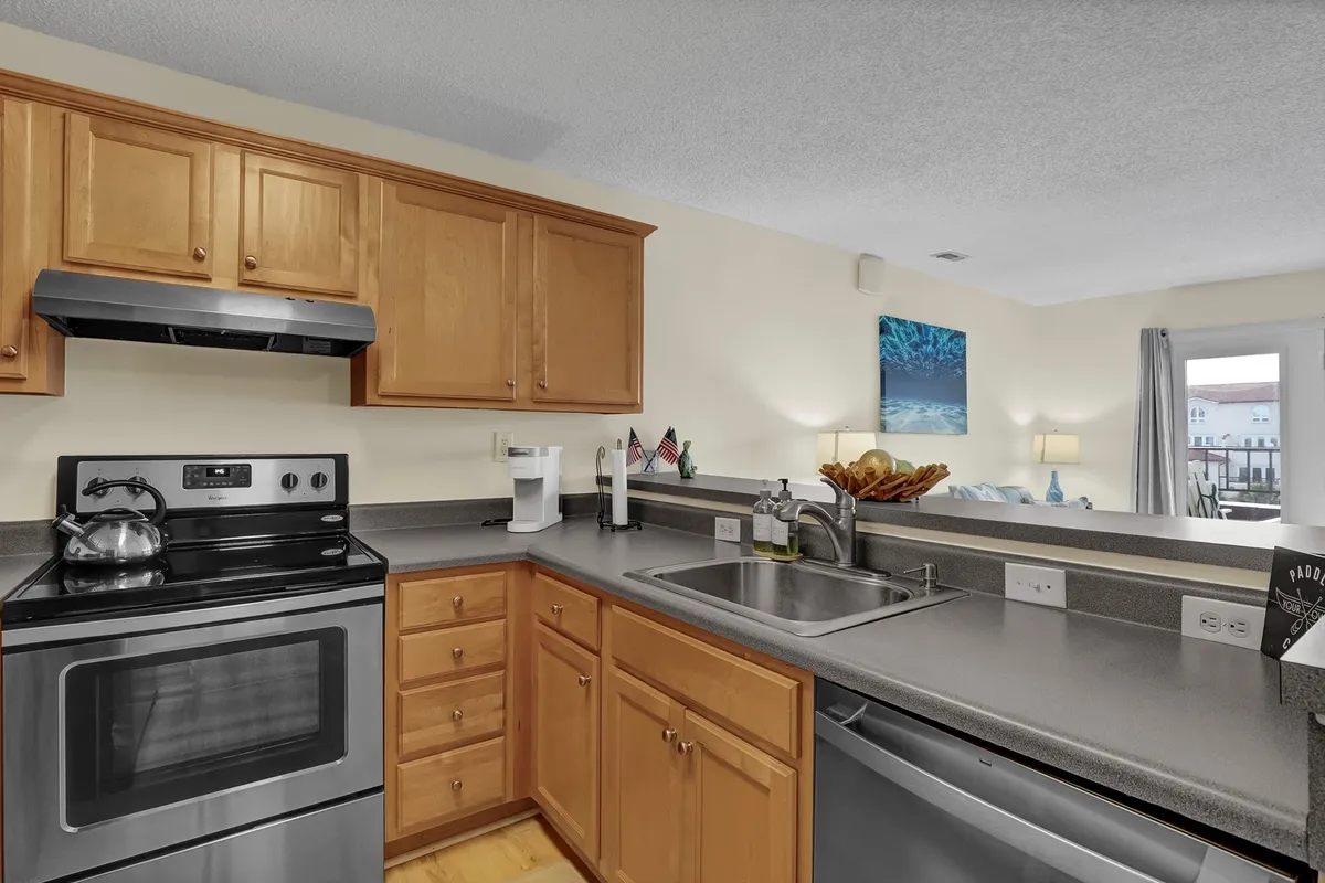 A close-up of a modern kitchen featuring stainless steel appliances, wooden cabinetry, and a sink with a window view. The setup is clean, functional, and ready for both casual snacks and elaborate meal prep.