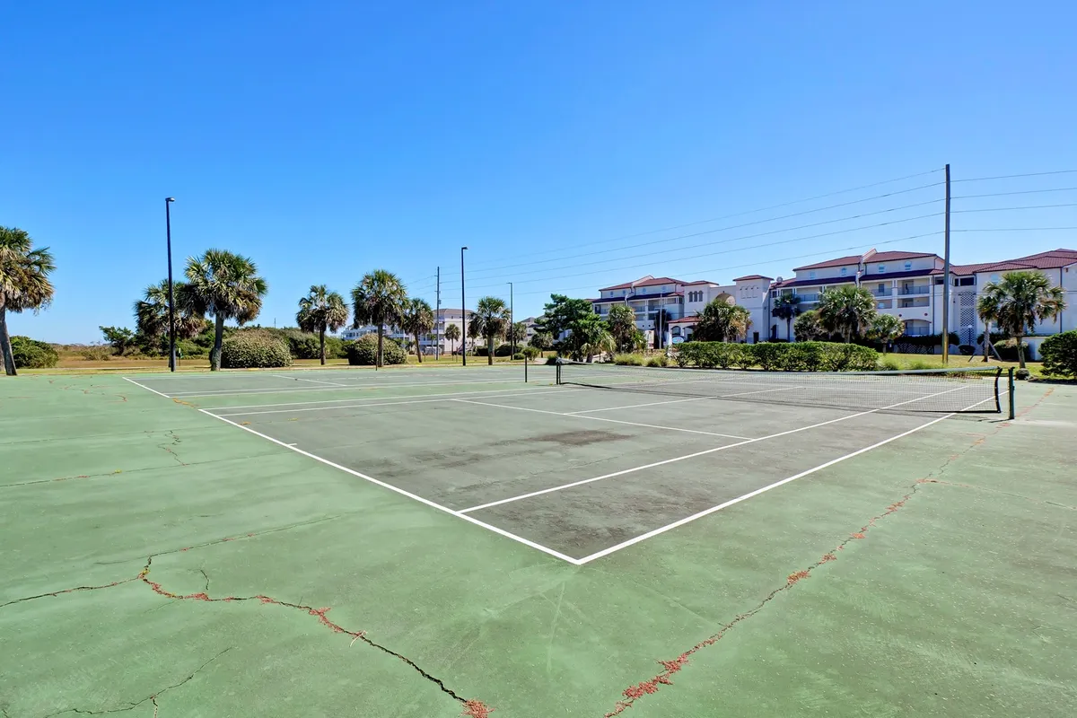 The image shows a well-maintained tennis court bordered by palm trees with the resort’s buildings in the background. The court is set up for friendly matches or casual play, capturing the energetic side of Villa Capriani’s amenities.