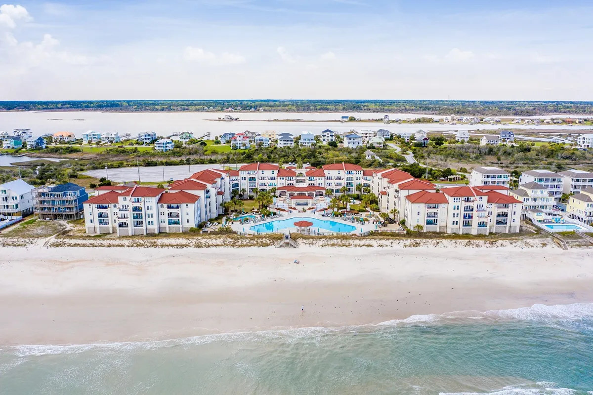 This image features a vibrant beachfront property with a spacious swimming pool, surrounded by residential buildings and an inviting sand beach meeting the ocean. The scene highlights areas for swimming, sunbathing, outdoor dining, and family gatherings, with the ocean as the backdrop.