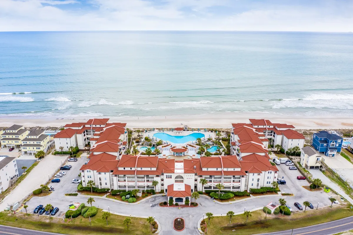 An exterior scene showcasing a lively swimming pool surrounded by resort buildings, manicured gardens, and the adjacent sandy beach. The inviting pool area is set with lounge chairs and palm trees, creating an energetic yet relaxed atmosphere for swimming and socializing.